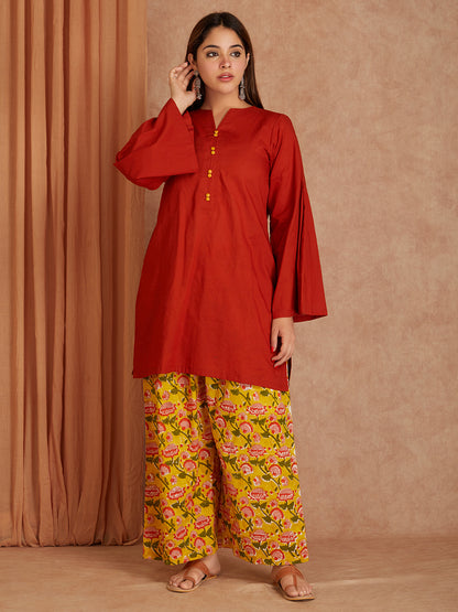 Woman wearing a red top and yellow floral pants against a brown background